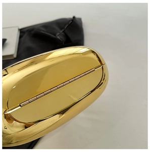 Macro view of polished gold metal evening clutch bag showing sleek bottom hinge detail