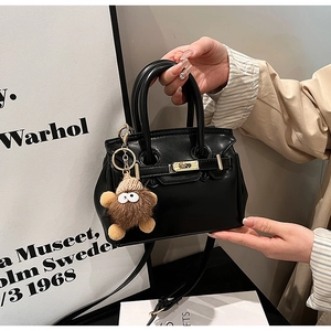 Detail of black pebbled leather handbag with gold twist lock and cute monster charm