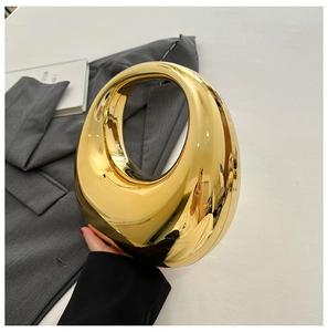 Detail of a crescent-shaped gold acrylic evening bag with a high-shine mirror finish