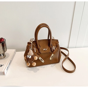 Macro view of brown Kelly bag's gold metal twist lock and cute plush doll pendant