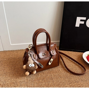 Detailed close-up of brown leather bag with golden twist lock and plush monster charm