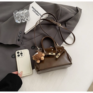 Close-up of coffee brown tote bag with plush bear charm in a chic urban office setting