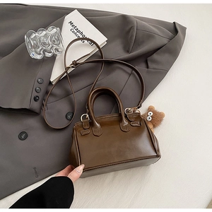 Detail of a dark brown crossbody bag with a plush bear charm and adjustable strap