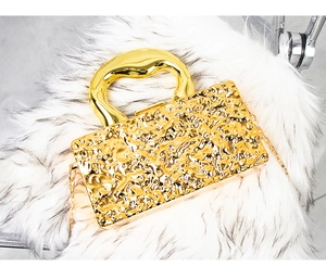 Detail of luxury gold evening clutch with textured lava pattern and curved metal handle