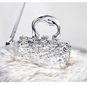Detail of silver metallic box bag with lava texture and arc handle on plush surface