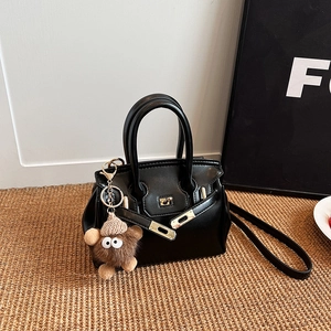 Classic black leather Kelly style handbag with gold lock and plush charm on a woven mat