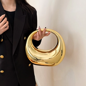 Golden crescent acrylic evening clutch bag with mirror finish held by model in suit