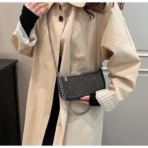 Close-up of black rhinestone saddle bag with chunky silver chain on a beige trench coat