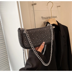 Close-up of black denim baguette bag with silver rivets and metal chain strap