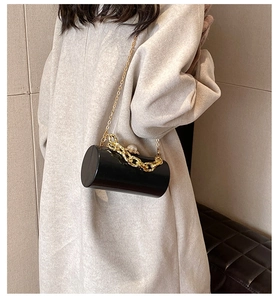 Detail of black cylindrical clutch bag with chunky gold chain handle and pearl clasp