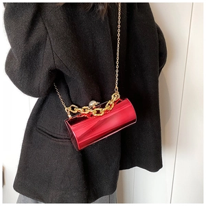 Macro detail of red cylindrical acrylic clutch with gold chain and pearl clasp button