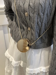 Dettaglio di una mini borsa a scatola tonda in metallo dorato con tracolla a catena