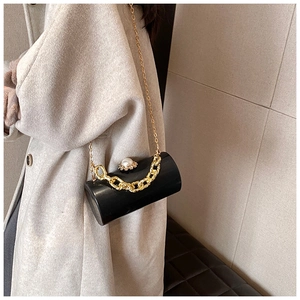 Detail of black acrylic cylinder bag featuring pearl clasp and gold chain straps