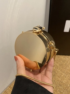 Dettaglio di una mini borsa a scatola tonda in oro con chiusura a ape e catena dorata