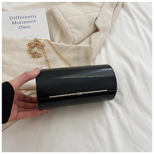 Detail view of a black acrylic cylinder clutch bag with golden chain and mirror finish