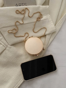 Vista dall'alto della mini borsa tonda dorata con catena a serpente e telefono per dimensioni