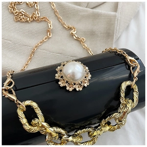 Macro view of black acrylic mirror cylinder bag with gold chain and pearl buckle
