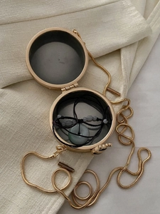 Dettaglio di una mini borsa tonda dorata con collana in giada e catena a serpente sottile