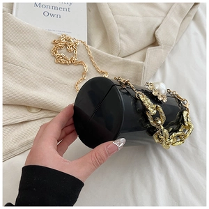 Detail of a black cylindrical clutch featuring pearl floral accents and golden chain