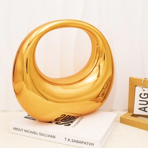 Macro view of a modern golden hollow circular ceramic vase on art books with smooth mirror finish