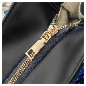 Détail du zip en métal doré et sequins colorés sur un sac à main en cuir noir grainé