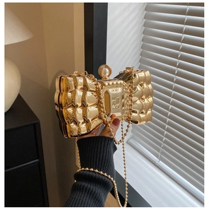 Detail of a golden bow-shaped evening clutch with embossed texture and pearl clasp