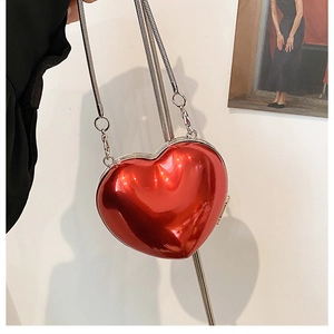 Detail of red heart shaped acrylic crossbody bag with silver snake chain held by hand