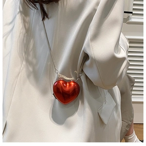 Mini red heart-shaped acrylic crossbody bag with silver chain on white suit model