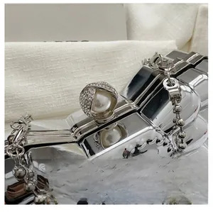 Close-up of wavy metallic clutch bag featuring a pearl and diamond encrusted clasp with ball chain