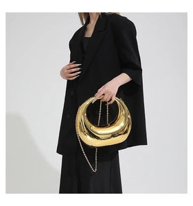 Close-up of golden moon-shaped evening bag with polished mirror finish and chain