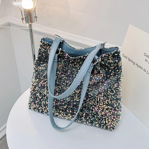 Sac fourre-tout à paillettes colorées avec poignées en cuir bleu sur une table blanche