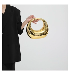 Detailed close-up of a golden mirror acrylic crescent evening bag held by a model
