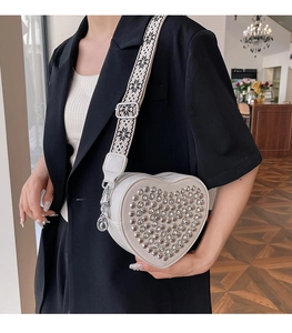 Détail du sac blanc en forme de cœur avec clous argentés et large bandoulière à motifs