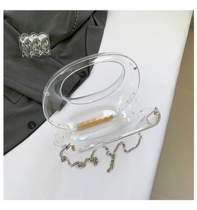 Detail of transparent crescent acrylic clutch with golden hinge and silver chain strap