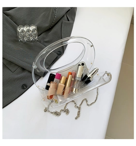 Macro view of transparent acrylic evening bag with metal chain showing interior cosmetics