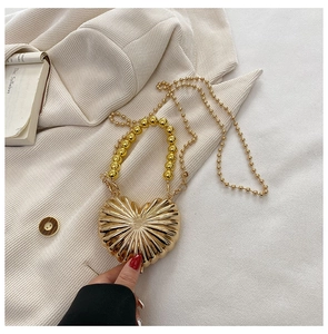 Detail of heart-shaped gold metal handbag with radial texture and beaded handle