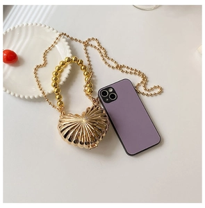 Detail of heart-shaped gold metal mini bag with bead handle and elegant chain strap