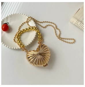 Macro detail of heart-shaped gold metal mini bag with radiant textured finish and chain