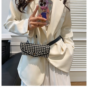 Détail d'un sac banane noir orné de strass et clous argentés sur un blazer blanc