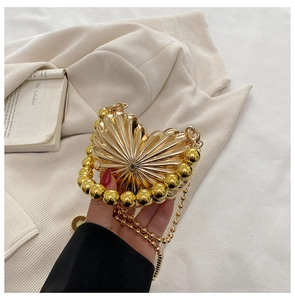 Detailed view of heart-shaped gold metal clutch with radial pleats and beaded edge
