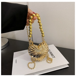 Detail of a golden heart-shaped metal evening bag with radial texture and beaded handle