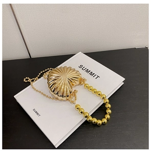 Detail of heart-shaped gold metal evening bag with ribbed texture and beaded handle