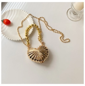 Detail of heart-shaped gold metal mini bag with radial texture and bead handle