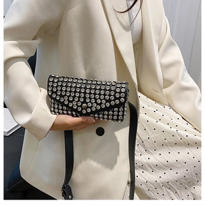 Détail d'un sac bandoulière noir avec strass argentés porté sur un blazer blanc