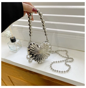 Macro detail of a heart-shaped silver metal bag with pleated texture and pearl handle