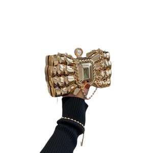 Golden bow-shaped acrylic clutch bag with large gem, pearl top, and quilted metal texture