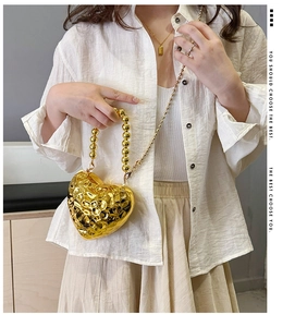 Detail of a gold heart-shaped acrylic clutch bag with bead handle and metallic texture