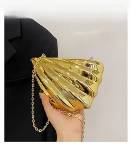 Detail of a golden seashell-shaped hard shell clutch bag with mirror-like finish and chain