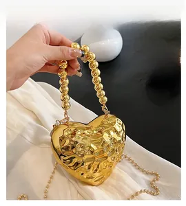 Close-up of golden heart-shaped evening bag with hammer-textured finish and beaded handle