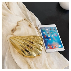 Macro shot of shell shaped gold evening clutch with sleek metallic finish and chain strap